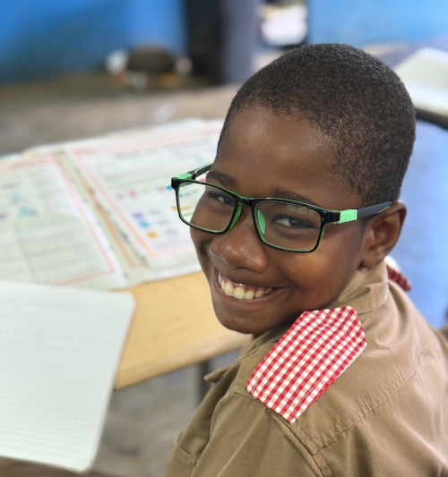 See Better.Learn Better Jamaica Young boy at desk in glasses, smiling