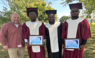 A photo of three graduates from the Haiti Optometry School holding certificates, and an instructor beside them.