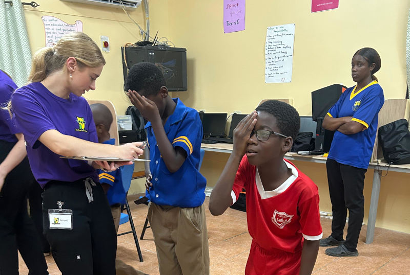 A photo of a child eye care project in Jamaica with two children looking at an eye chart in a school gymnasium.